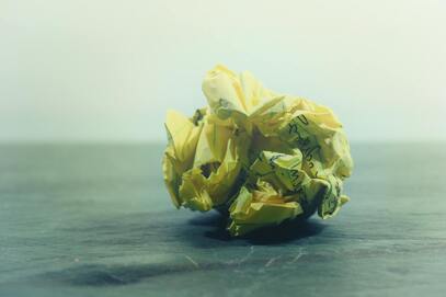 picture of crumpled up ball of  yellow legal paper with writing on it. 